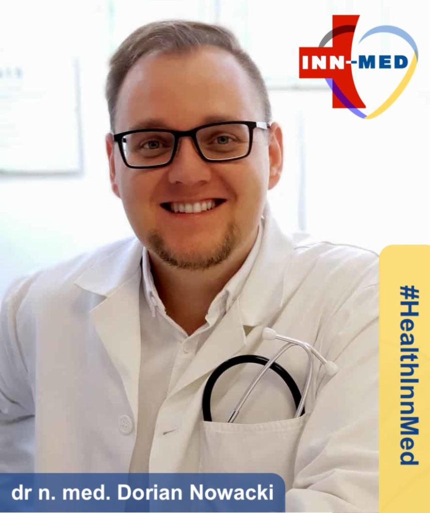 Uśmiechnięty doktor Dorian Nowacki z Wrocławia w białym fartuchu z logiem Inn-Med i stetoskopem w kieszeni.