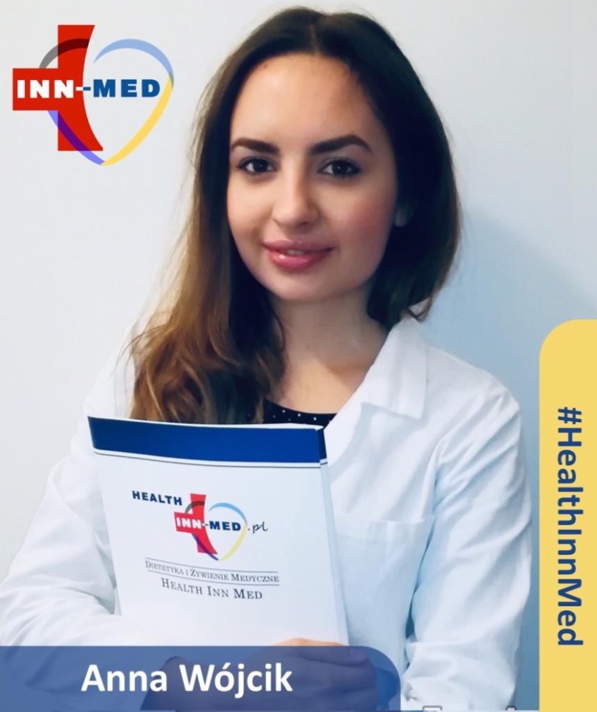 Portret uśmiechniętej kobiety w białym fartuchu medycznym, trzymającej w rękach folder z logo i nazwą 'Health Inn Med' oraz informacją 'Dietetyka i żywienie medyczne'. W tle widoczne logo firmy.