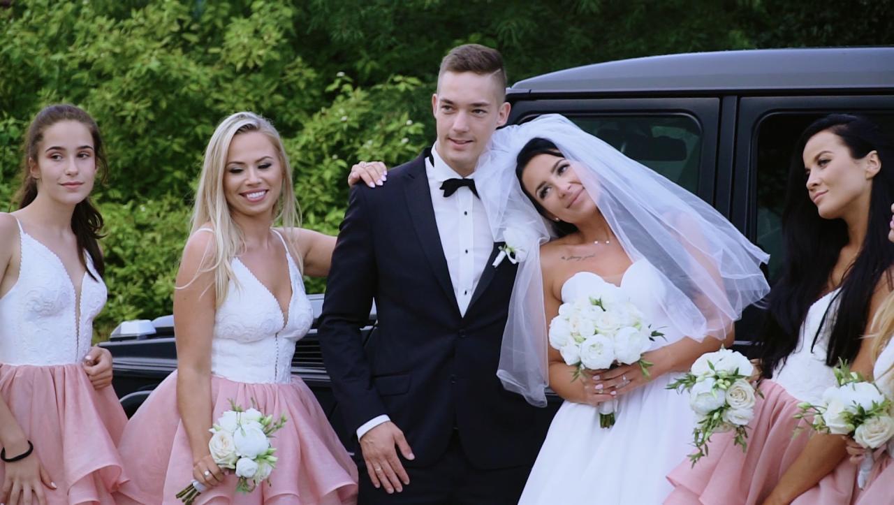 Uśmiechnięta para młoda w otoczeniu druhen pozuje przy czarnym samochodzie terenowym w dniu ślubu.