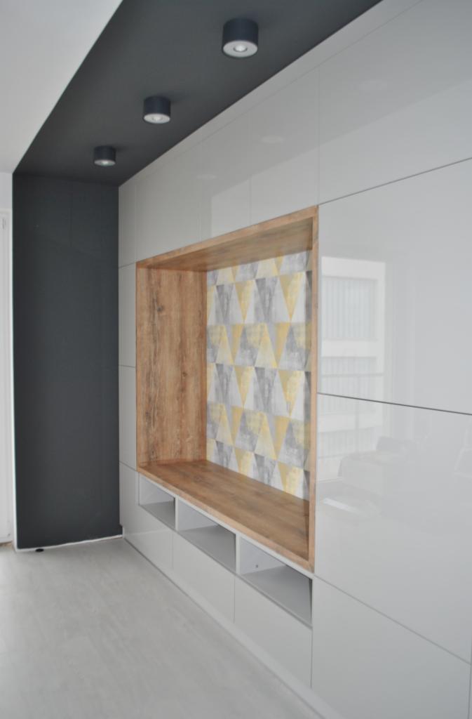 Biała szafa wnękowa z drewnianą wnęką wykończoną tapetą w geometryczne wzory, oświetlenie sufitowe punktowe.