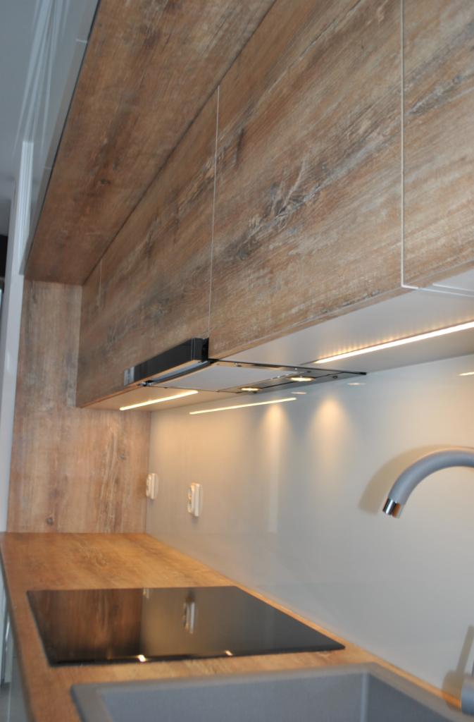 Nowoczesna kuchnia z drewnianymi frontami szafek górnych, oświetleniem LED podszafkowym i czarną płytą indukcyjną na blacie.