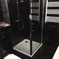 Nowoczesna kabina prysznicowa z brodzikiem, czarne płytki na ścianach i podłodze, chromowana armatura, grzejnik drabinkowy w łazience.