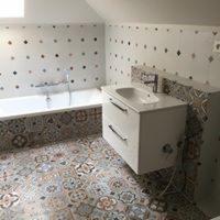 Jasna łazienka na poddaszu z wanną i umywalką w szafce, wzorzyste płytki na podłodze i ścianach z dekoracyjnymi wstawkami, chromowana bateria wannowa.