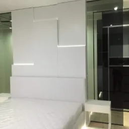 Nowoczesna sypialnia z białym łóżkiem, podświetlanym od dołu, z geometrycznym panelem ściennym z wbudowanym oświetleniem LED i lustrzaną szafą.