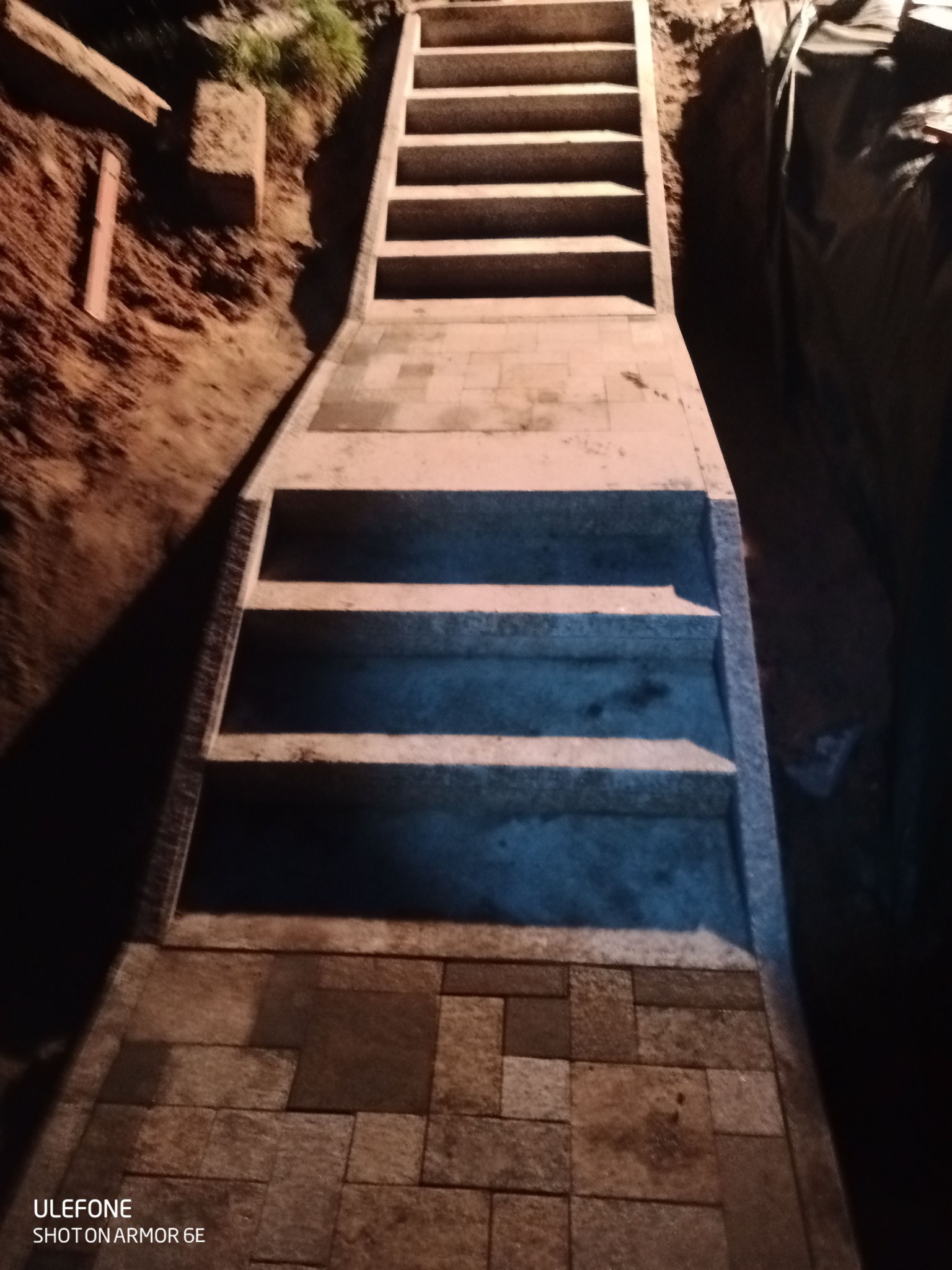 Granitowe schody zewnętrzne prowadzące w górę, wykonane z kostki w różnych odcieniach brązu i szarości, oświetlone ciepłym światłem w Jaworznie.