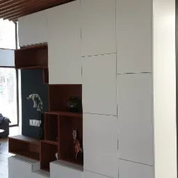 Nowoczesna szafa na wymiar z białymi frontami i otwartymi półkami z ciemnego drewna, element dekoracyjny w postaci figurki i wazonu, widoczny fragment drewnianego sufitu