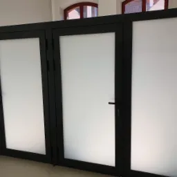 Czarne, aluminiowe drzwi z matowym szkłem w nowym budynku, widoczne fragmenty okien na górze