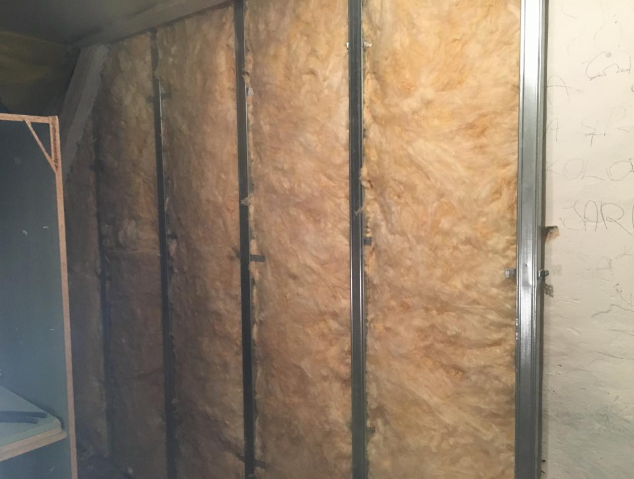 Metalowy stelaż z wełną mineralną, przygotowany pod montaż płyt kartonowo-gipsowych, widoczne ślady ołówka na ścianie obok.