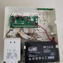 Otwarta obudowa centrali alarmowej z widoczną płytą główną Satel Perfecta 16, transformatorem Pulsar AWT468, akumulatorem MegaBat MB 7.2-12 oraz okablowaniem.