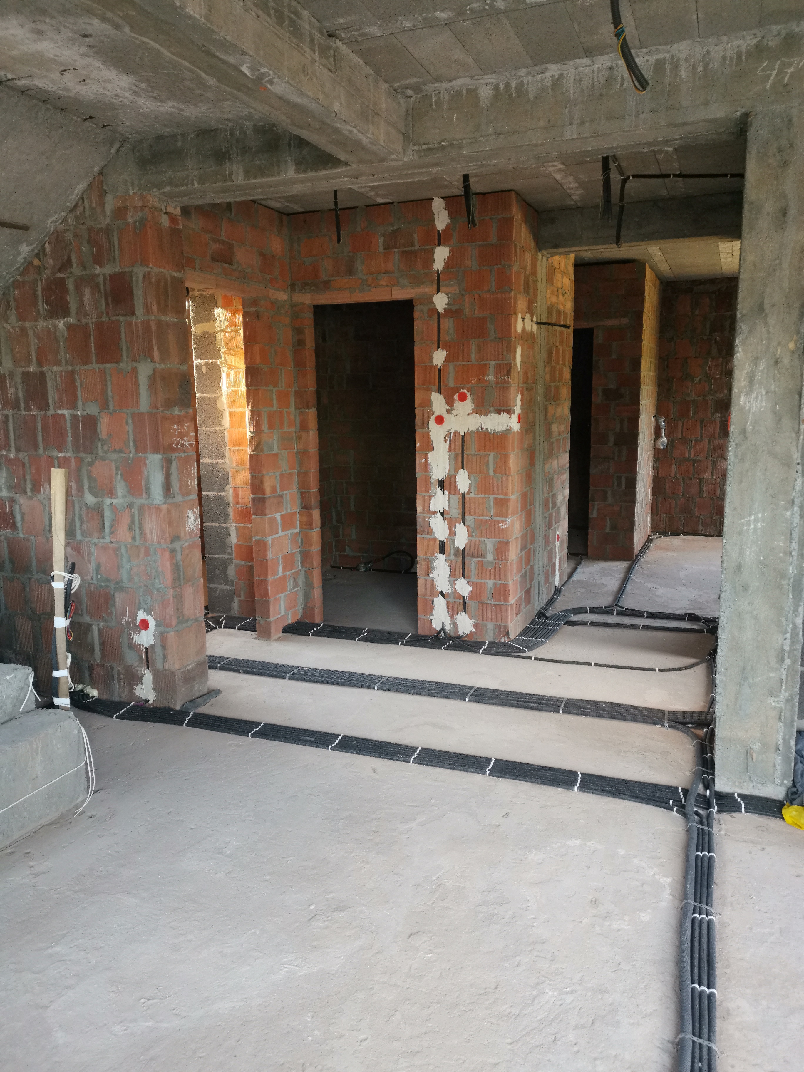 Wnętrze w trakcie prac wykończeniowych z widocznymi przewodami elektrycznymi prowadzonymi po podłodze i ścianach, zabezpieczonymi białymi opaskami.