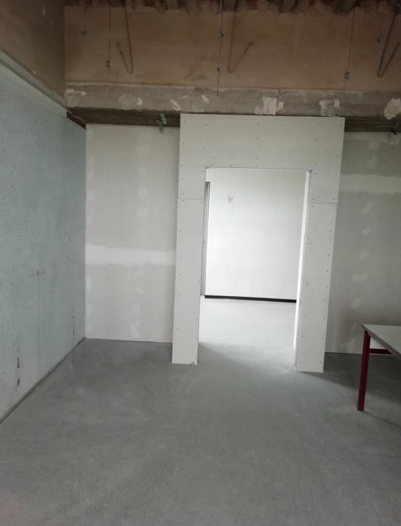 Montaż ościeżnicy z płyty karton gips, widoczne mocowania do sufitu i szpachlowane łączenia płyt na ścianach.