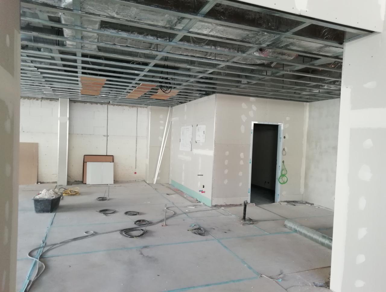 Montaż metalowej konstrukcji sufitu podwieszanego i płyt kartonowo-gipsowych w surowym pomieszczeniu z widocznymi przewodami i narzędziami.