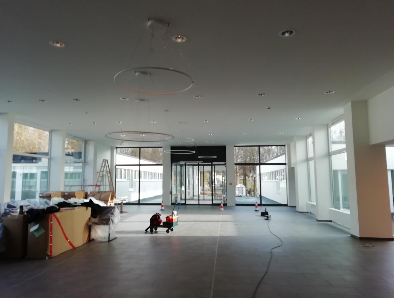 Przestronne wnętrze w trakcie montażu sufitu podwieszanego z widocznymi okrągłymi lampami, materiałami budowlanymi i narzędziami.