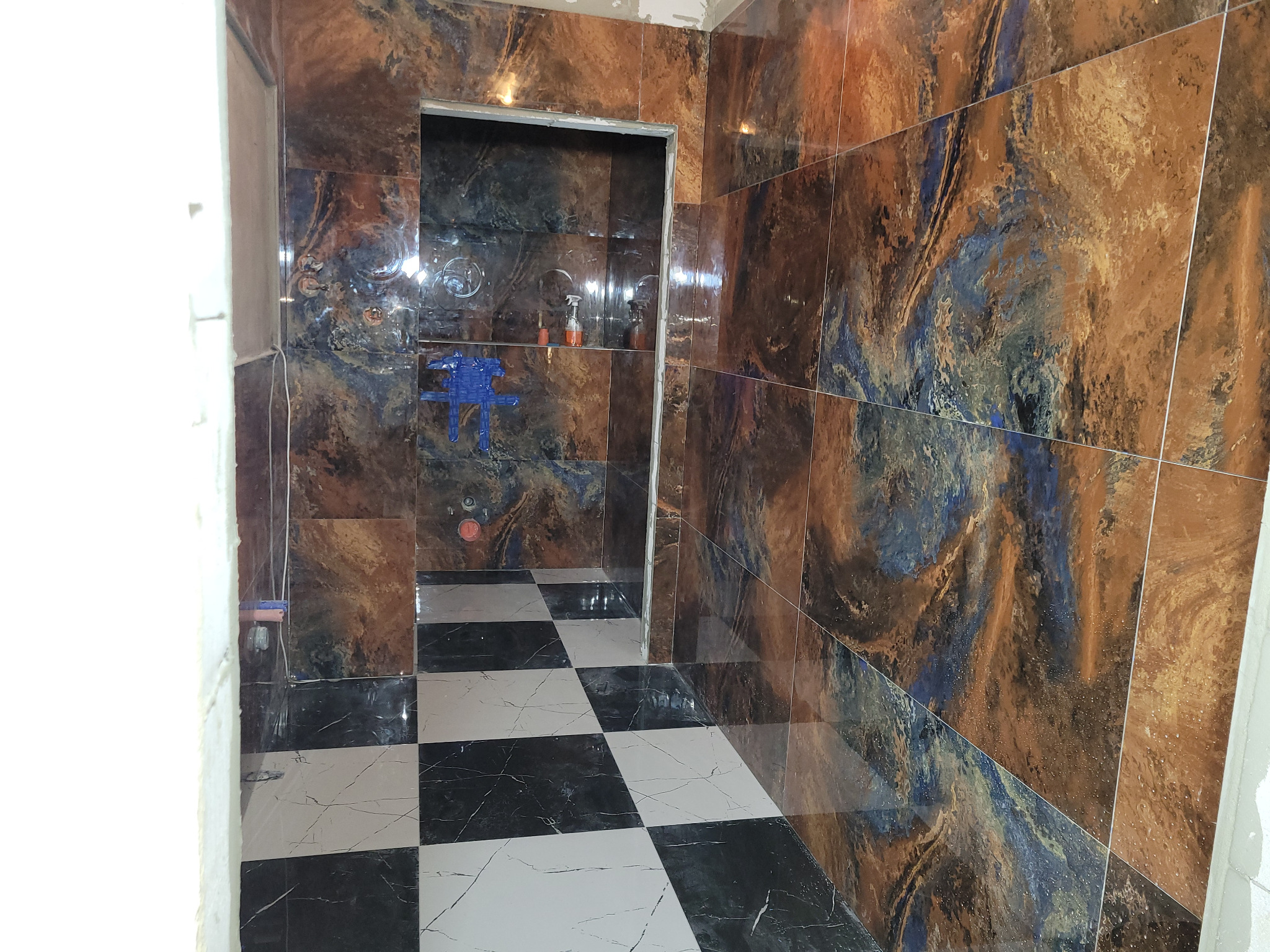 Wykończona łazienka z błyszczącymi, wzorzystymi brązowo-niebieskimi płytkami na ścianach i podłodze w szachownicę. Widok na kabinę prysznicową.