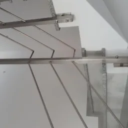 Minimalistyczna konstrukcja schodów z szarego granitu z metalową balustradą ze stali nierdzewnej, widok z dołu na jasne wnętrze.