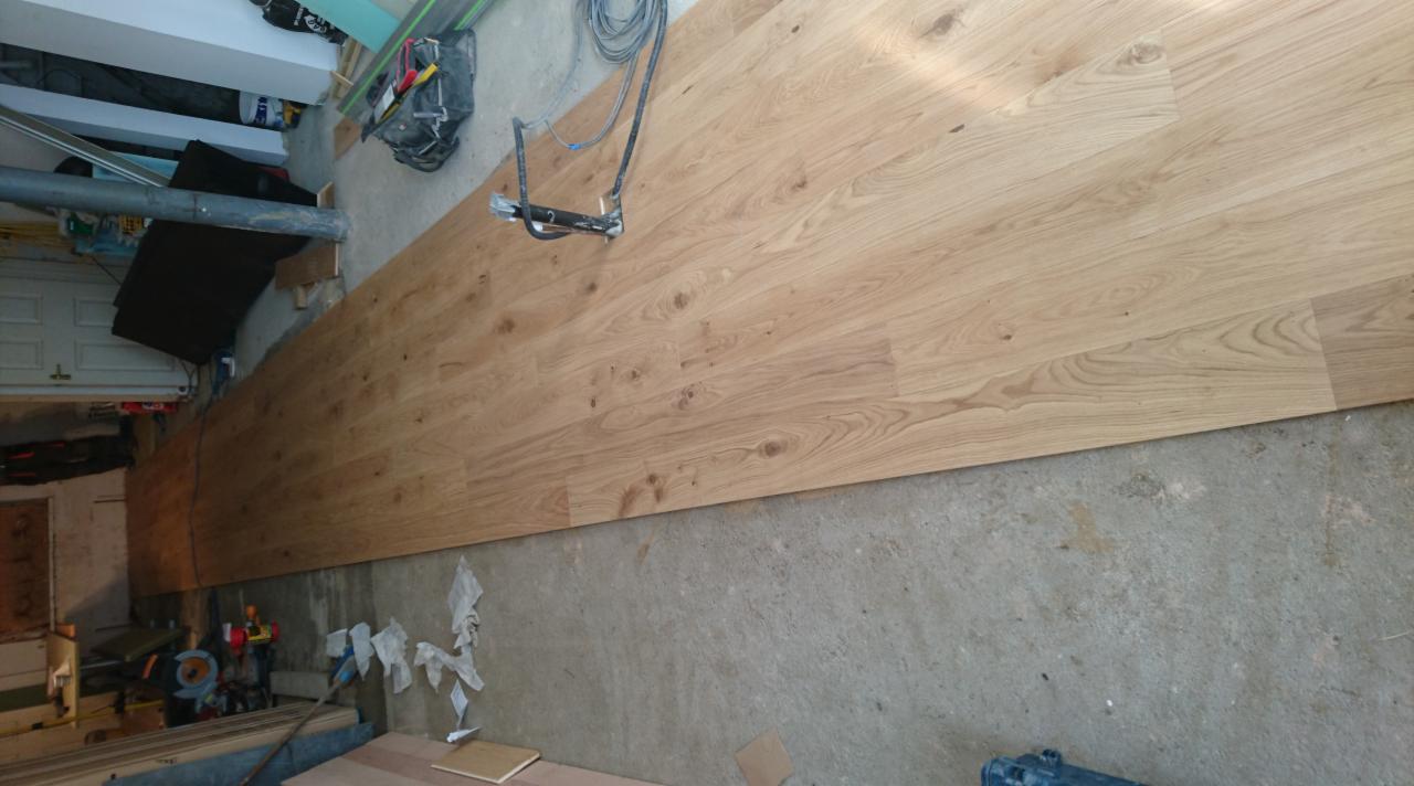 Układanie paneli podłogowych o jasnym odcieniu drewna na surowym, betonowym podłożu w trakcie prac remontowych. Widoczne narzędzia i akcesoria montażowe.