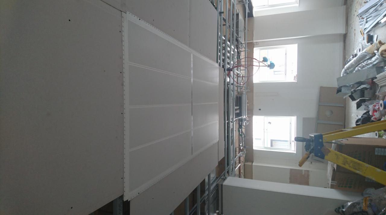 Montaż płyt gipsowo-kartonowych na metalowym stelażu w trakcie prac wykończeniowych w jasnym pomieszczeniu z oknami.