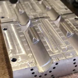 Metalowa forma wtryskowa z precyzyjnymi wgłębieniami i otworami, widoczna tekstura obróbki skrawaniem, ustawiona na warsztatowym stole.