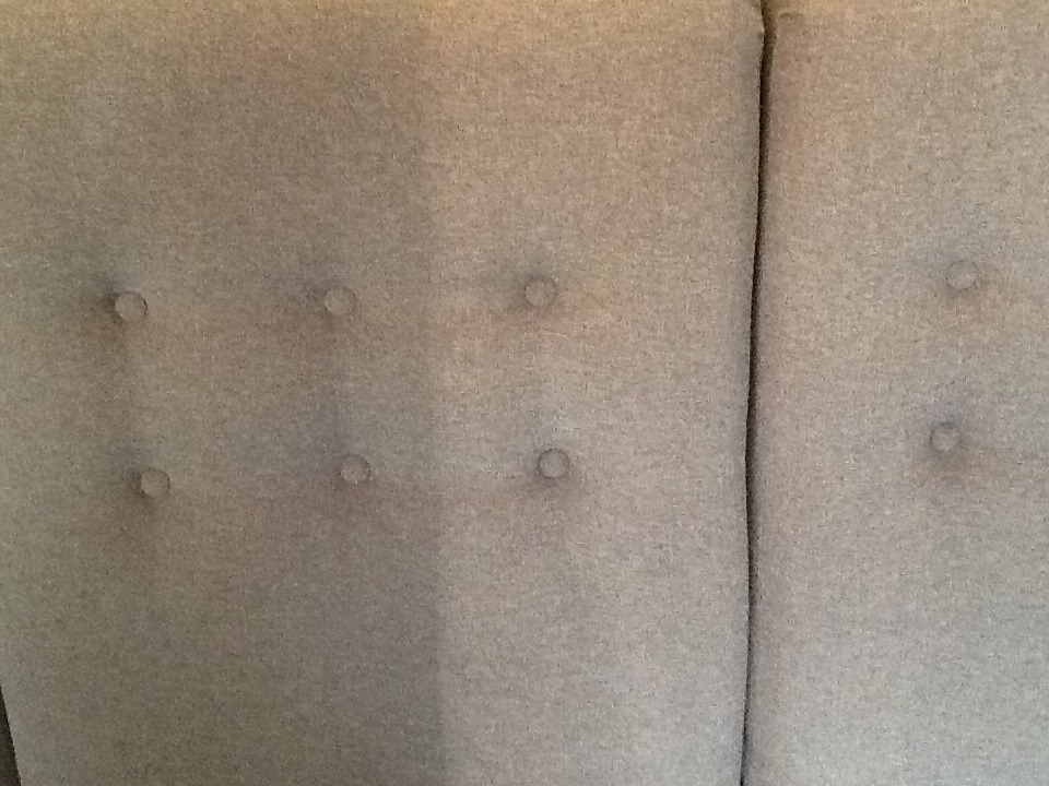 Fragment szarej tapicerki kanapy z guzikami, widoczny szew pionowy.