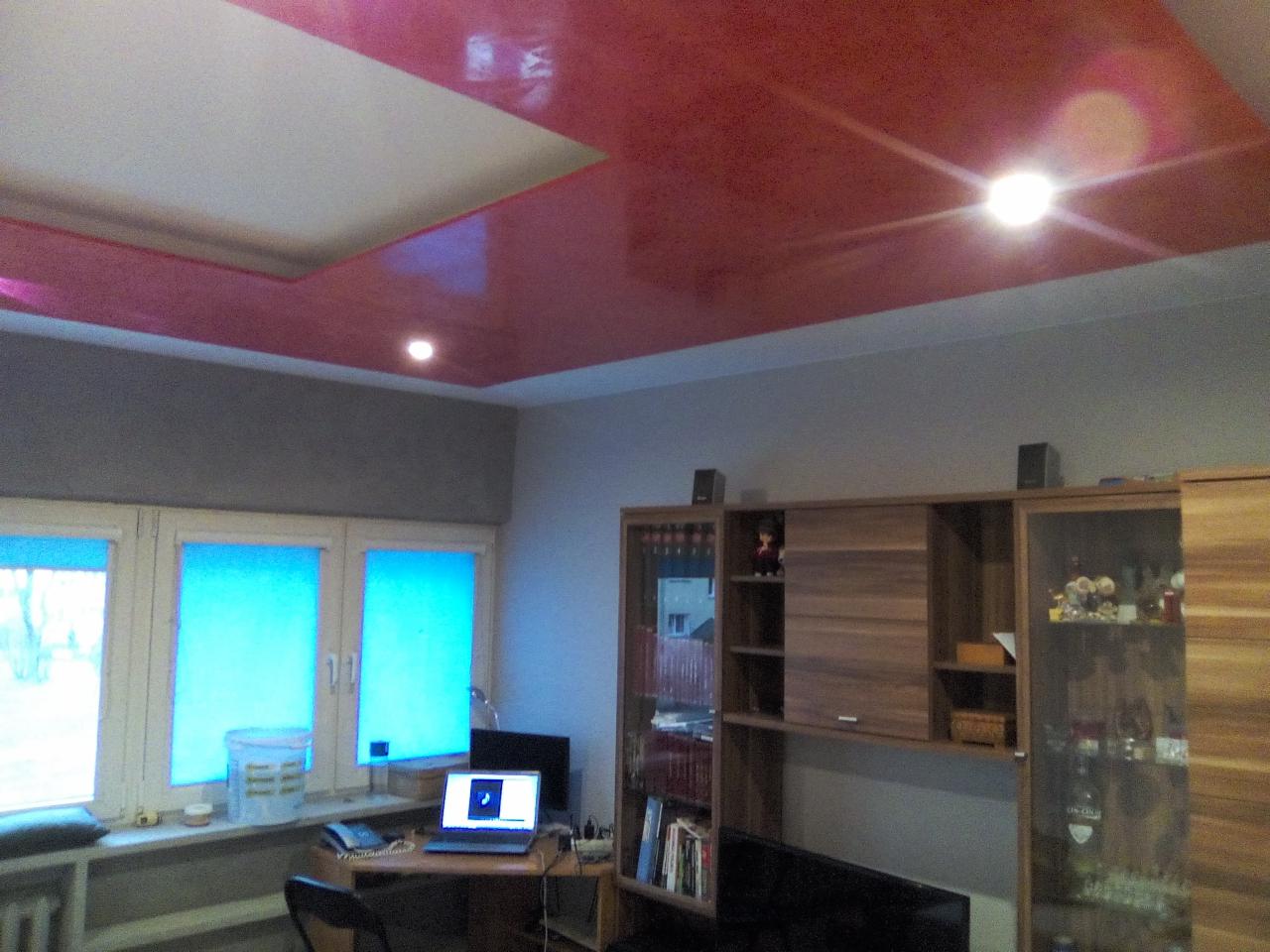 Pokój z błyszczącym, czerwonym sufitem podwieszanym z wbudowanym oświetleniem punktowym, szarymi ścianami i meblami z drewna w kolorze orzecha.