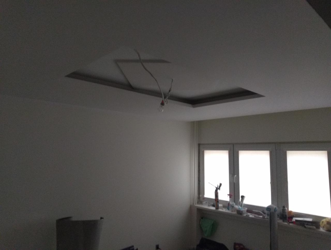 Niedokończony sufit podwieszany z widocznymi przewodami i ramą, wnętrze pokoju z oknem i narzędziami na parapecie