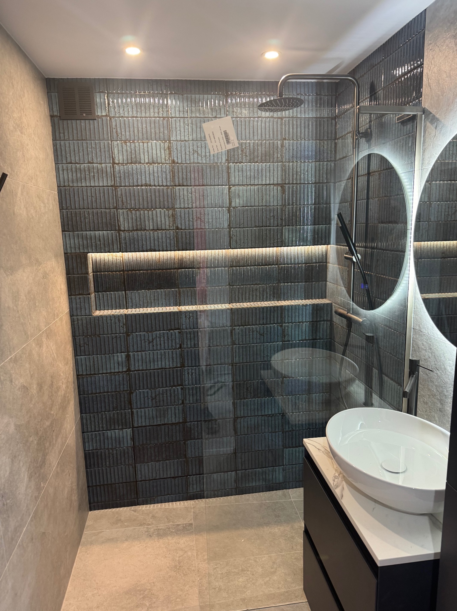 Nowoczesna kabina prysznicowa z deszczownicą i podświetlaną półką w Bytomiu, wykończona pionowymi, strukturalnymi płytkami w odcieniach szarości i granatu, z okrągłym lustrem z podświetleniem LED...