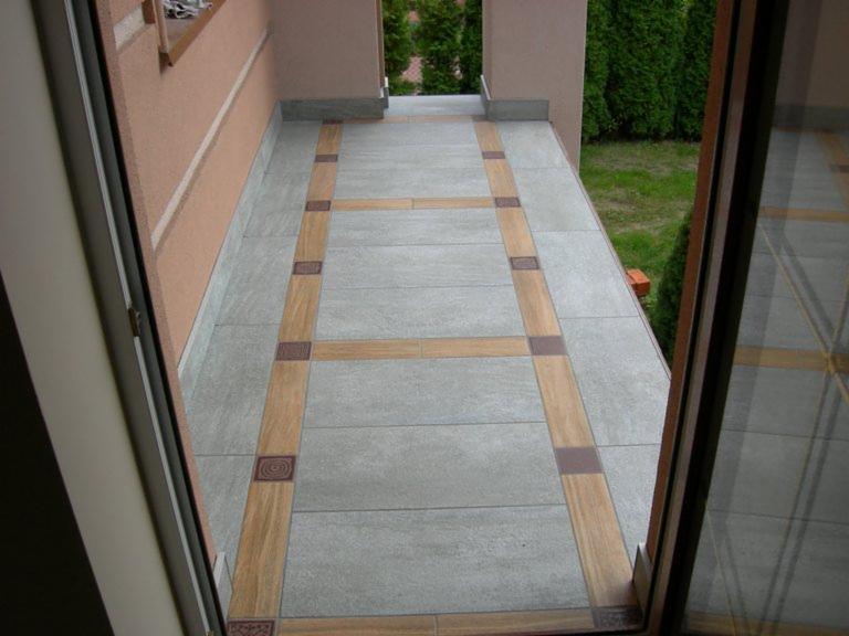 Wyłożony płytkami balkon z dekoracyjnymi wstawkami w odcieniach brązu i beżu, widok z wnętrza przez otwarte drzwi balkonowe.