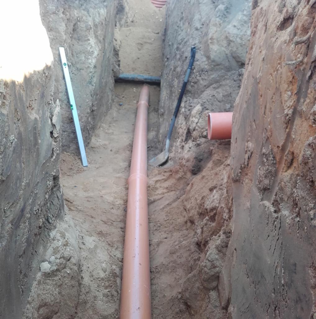 Wykop z ułożoną rurą kanalizacyjną z tworzywa sztucznego, poziomica i łopata w tle, widok z góry.