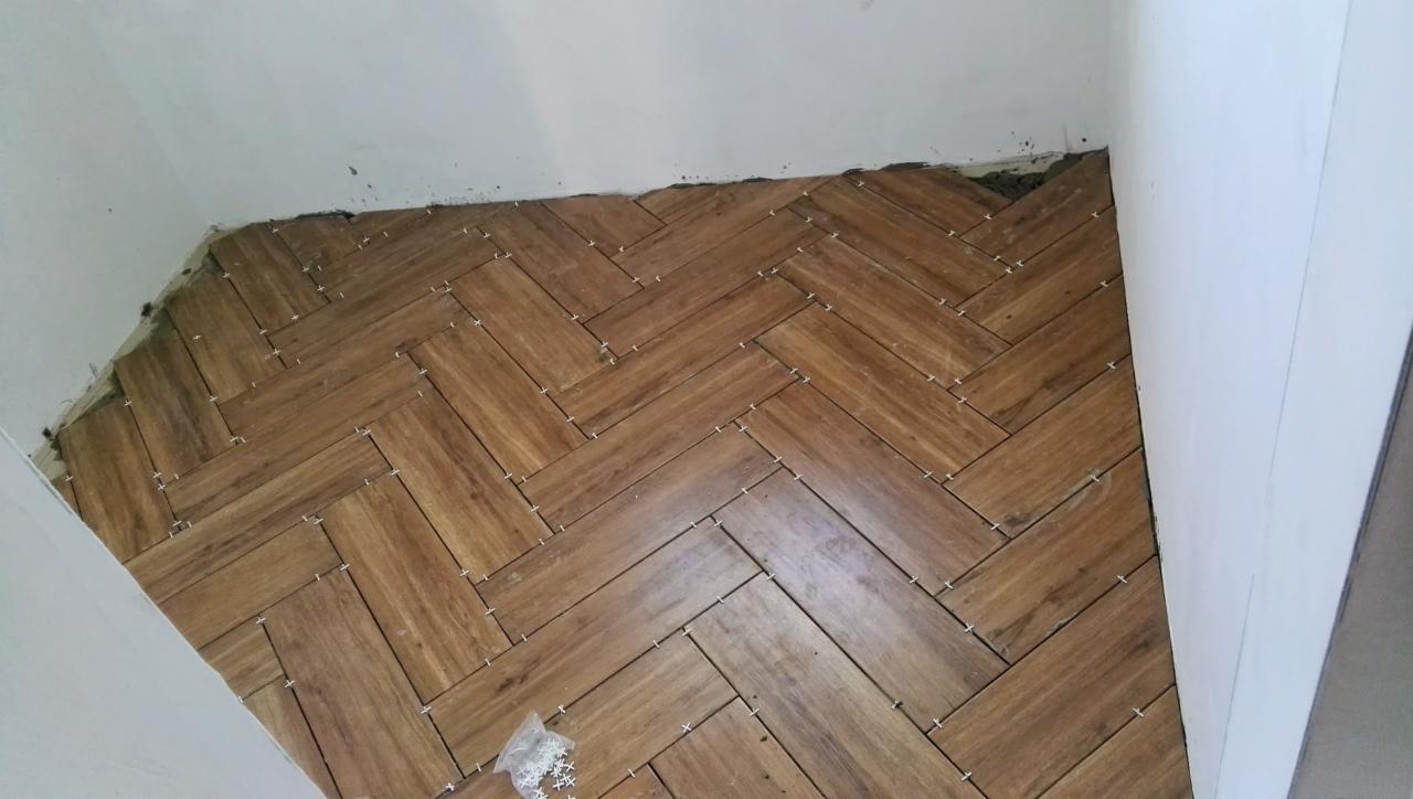 Układanie drewnopodobnej podłogi w jodełkę, widoczne krzyżyki dystansowe, ściany w trakcie wykończenia.