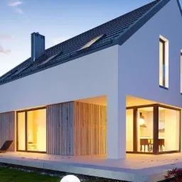 Nowoczesny dom jednorodzinny z płaskim dachem i dużymi przeszkleniami, oświetlony kulistymi lampami ogrodowymi o zmierzchu. Widoczne detale wykończenia elewacji.