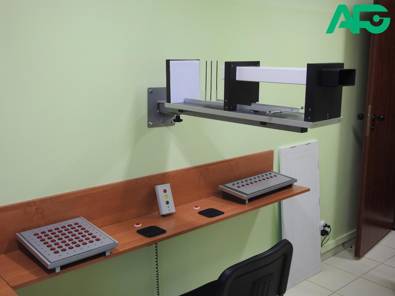 Aparat do badania widzenia stereoskopowego i koordynacji wzrokowo-ruchowej, z panelami kontrolnymi na drewnianym blacie i logo w rogu.