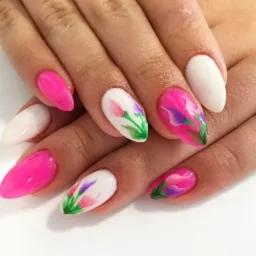 Dłonie z pomalowanymi paznokciami: niektóre w kolorze białym i różowym, inne zdobione motywem kwiatowym w odcieniach różu, fioletu i zieleni na białym tle.