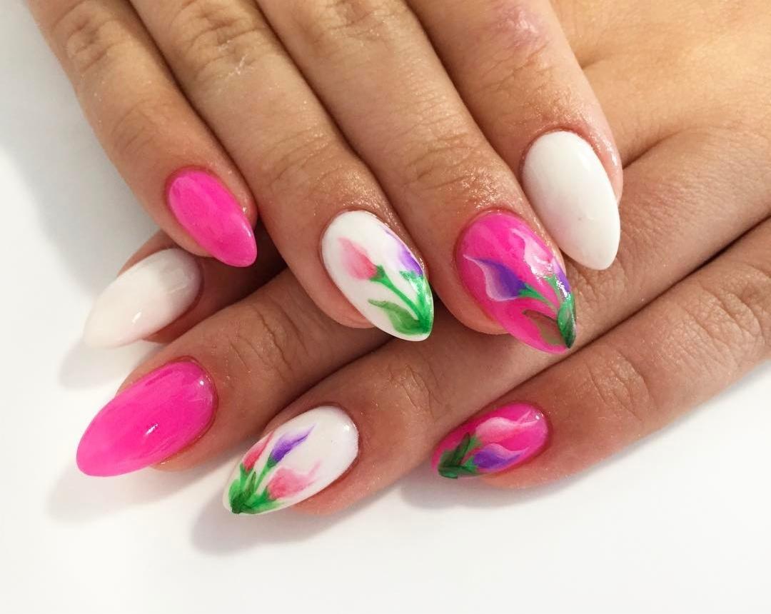 Dłonie z pomalowanymi paznokciami: niektóre w kolorze białym i różowym, inne zdobione motywem kwiatowym w odcieniach różu, fioletu i zieleni na białym tle.