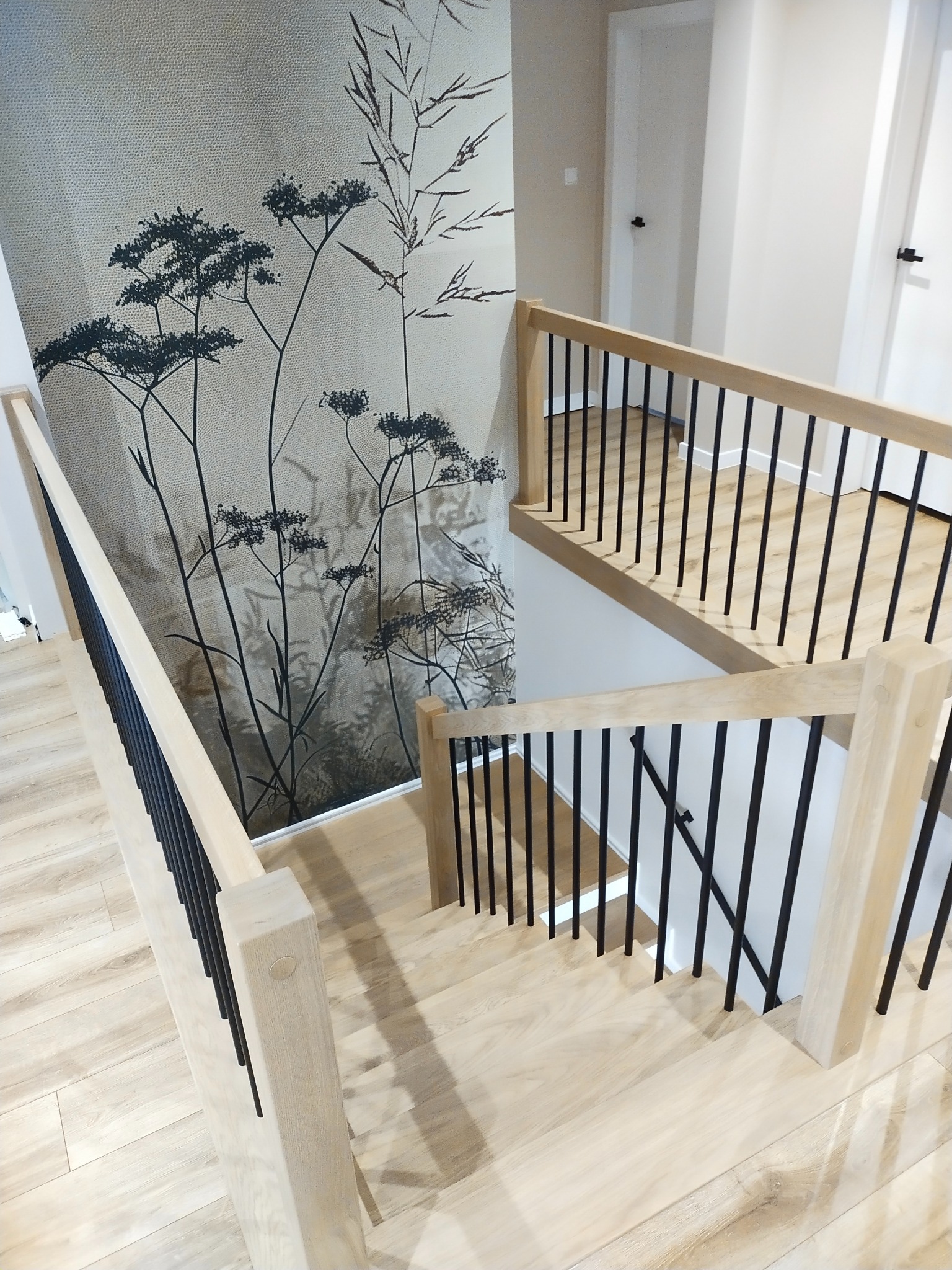 Jasne, nowoczesne schody z drewnianymi stopniami i czarnymi, metalowymi balustradami, widok z góry, z dekoracyjną tapetą w tle.