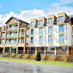 Nowoczesny budynek hotelowy z balkonami i przeszklonymi balustradami, widok z ulicy w słoneczny dzień.