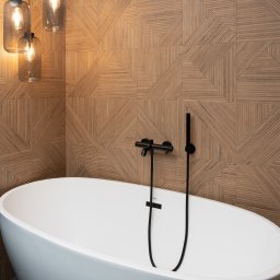 Triangle Studio - Nowoczesna łazienka: wolnostojąca wanna, geometryczna ściana z drewnopodobnych płytek, czarna armatura i wiszące lampy z żarówkami Edisona.