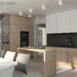 Nowoczesna kuchnia z drewnianymi szafkami i białymi górnymi szafkami, czarnym blatem i wyspą kuchenną z owocami, oświetlona kwadratowymi lampami sufitowymi.