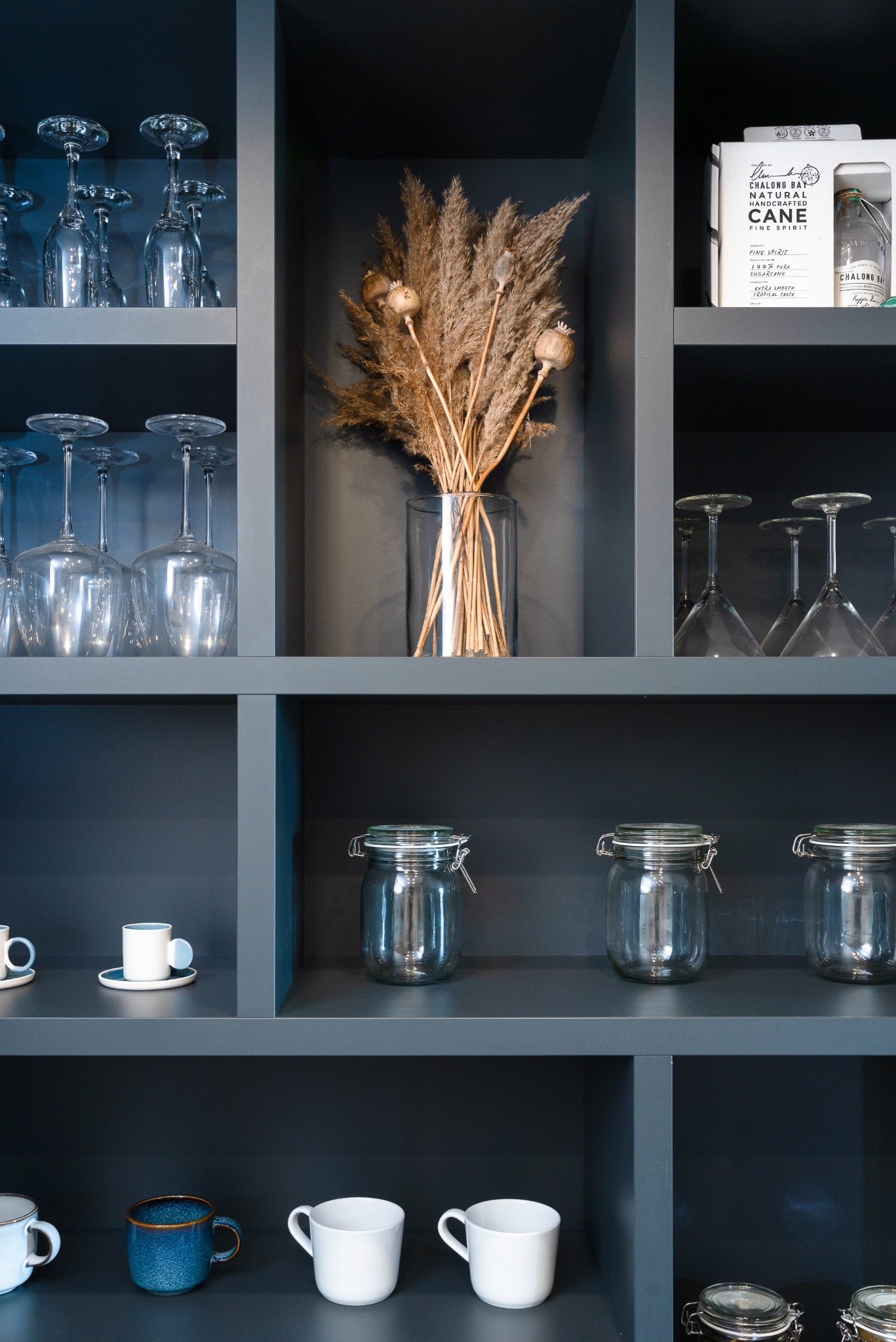 Stylowa zabudowa meblowa z dekoracjami w Dobczycach: szklanki, słoiki, wazon z suszem i butelka alkoholu. Minimalistyczny design, ciemne tło, eleganckie detale.