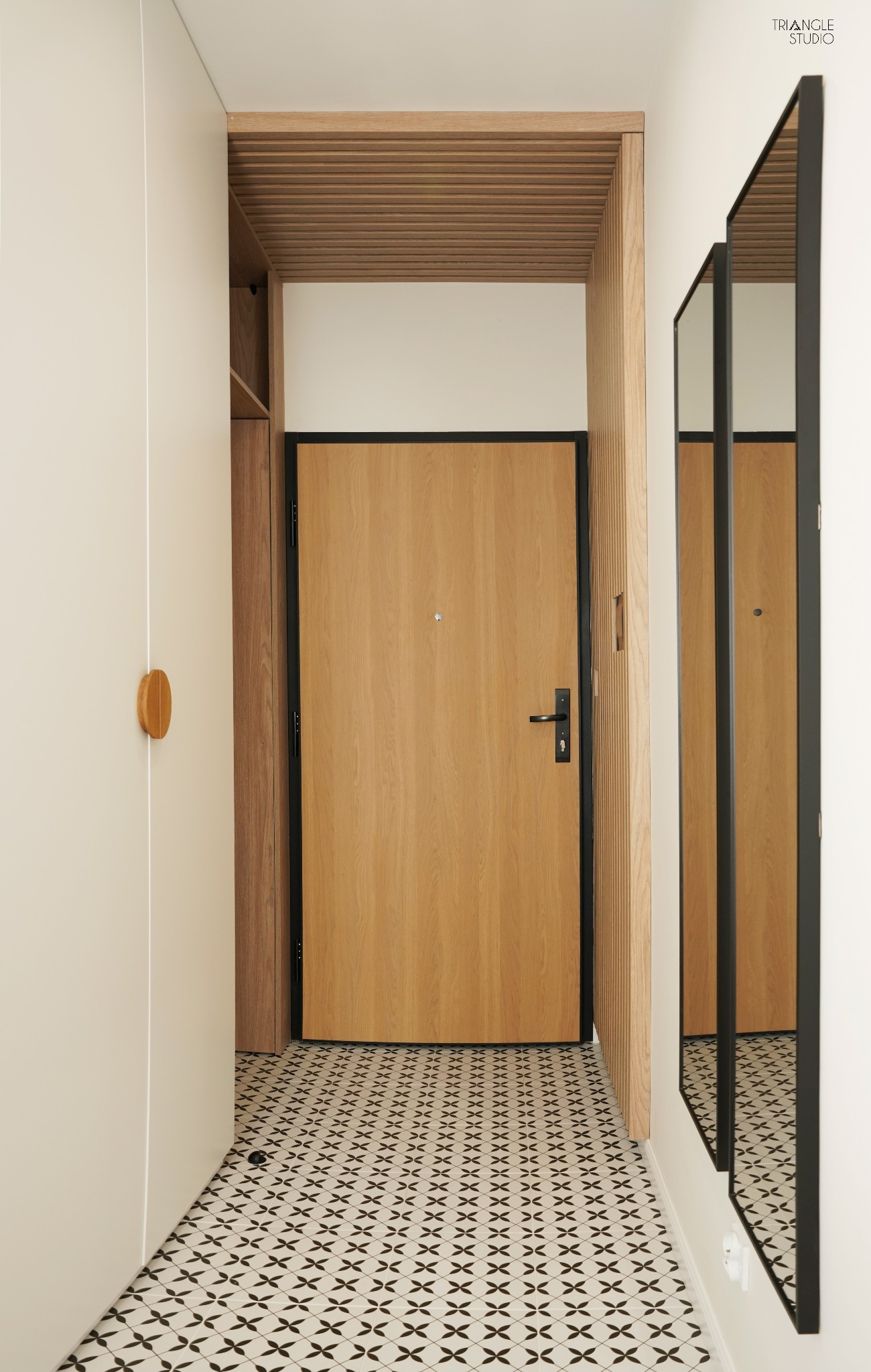 Nowoczesny przedpokój z drewnianymi akcentami: drzwi z czarną ramą, lustro w czarnej ramie, wzorzysta podłoga i drewniane lamele na suficie.