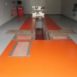 Pomarańczowa posadzka w warsztacie samochodowym z kanałem naprawczym i szarą strefą wok&oacute;ł, widok z g&oacute;ry na gładką powierzchnię.