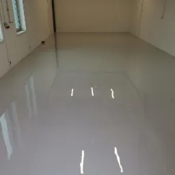 Świeżo wylana, jasnoszara, gładka posadzka z żywicy w pustym pomieszczeniu z oknami, widoczne refleksy światła.
