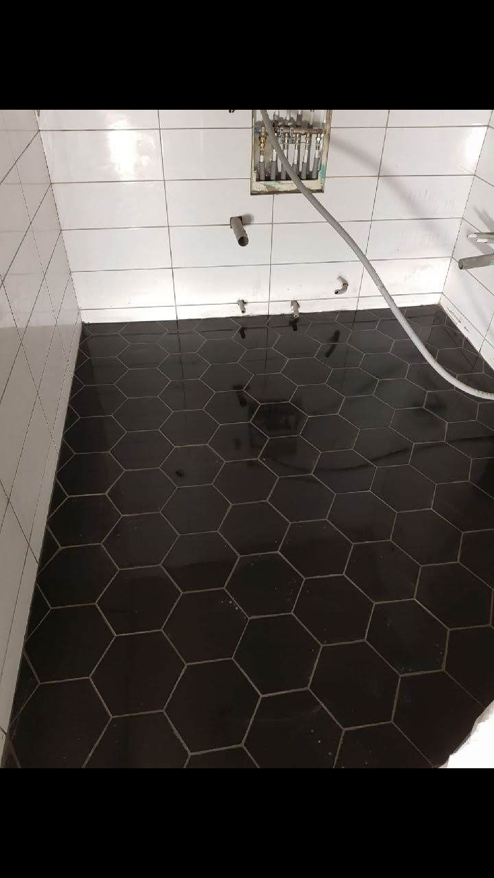 Czarne, heksagonalne płytki podłogowe w łazience w trakcie remontu, widoczne białe płytki ścienne i wystające rury instalacji wodnej.