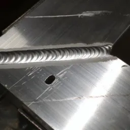 Spoina aluminium wykonana metodą TIG, widoczne regularne fale i niewielki otw&oacute;r obok spoiny.