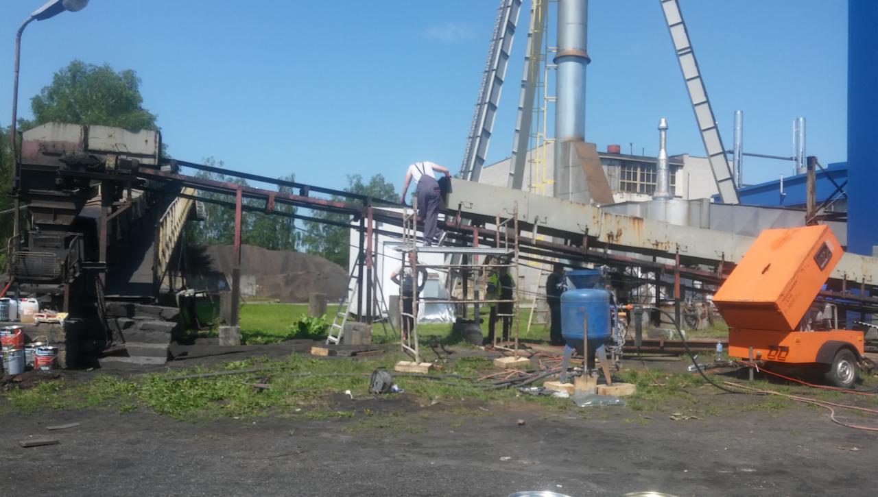 Prace przygotowawcze do piaskowania konstrukcji przemysłowej w Leżajsku: pracownik na rusztowaniu, agregat piaskarski i zbiornik, widoczne ślady korozji na elementach.