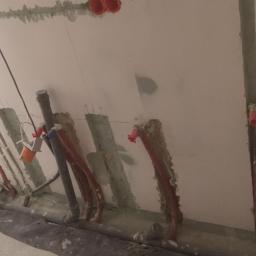 LUX GROUP SPÓŁKA Z O.O. - Wykute bruzdy w ścianie pod instalację elektryczną i rury, widoczne przewody, rury PEX, resztki gruzu i wiertarka udarowa.