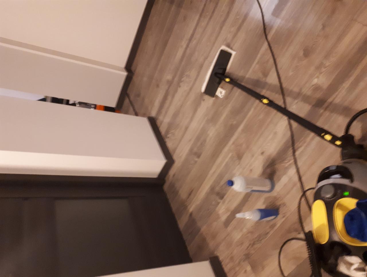 Parownica z żółtymi akcentami i mopem na drewnianej podłodze, obok butelki z płynem czyszczącym, widok z góry.