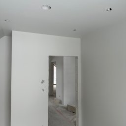 TERMOIZOLACJA - Dawid Wysocki - Wnętrze po szpachlowaniu i malowaniu na biało, widoczne otwory na oświetlenie w suficie i surowe wykończenie ościeżnic. Minimalistyczny efekt wykończenia.