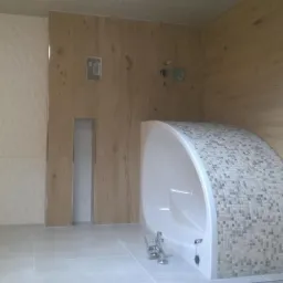 Nowoczesna łazienka z wanną obudowaną mozaiką, drewnopodobnymi panelami ściennymi i płytkami o trójwymiarowej strukturze na ścianie.