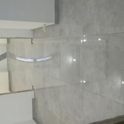 Cis-Bud - Świeżo położone, błyszczące, szare płytki na ścianie w pomieszczeniu w Mokrzyskach, z widocznym fragmentem sufitu i przygotowaną podłogą.