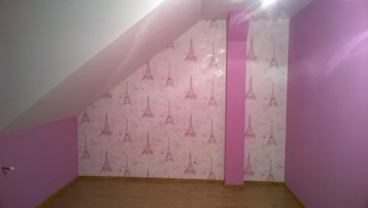 Poddasze po remoncie, ściany pomalowane na fioletowo i pokryte tapetą w wieże Eiffla, widoczny skośny sufit.